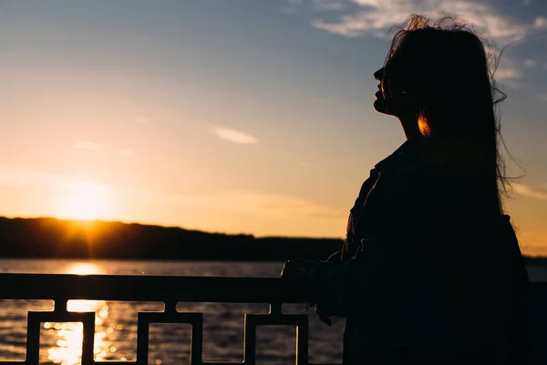 Silhouette de fille près de la clôture du lac et le coucher du soleil. de près. profil — Photo