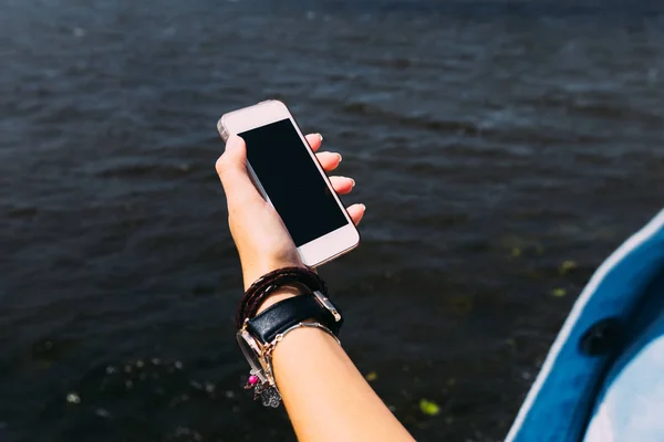hand of woman holding smart phone on  the backdrop of the lake.