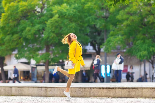 Het meisje in een gele vacht en handtas springt op de straat van de — Stockfoto