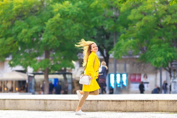 La fille en manteau jaune et sac à main court dans la rue de la — Photo