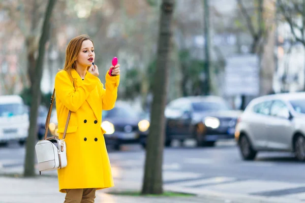 Niña en un abrigo amarillo con un bolso de mano que aplica lápiz labial en el pt — Foto de Stock