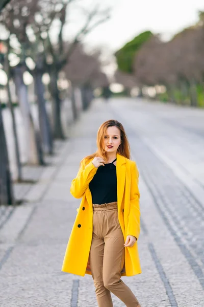 Portrait of a girl in a yellow coat walking in street. Female fa — Stock Photo, Image