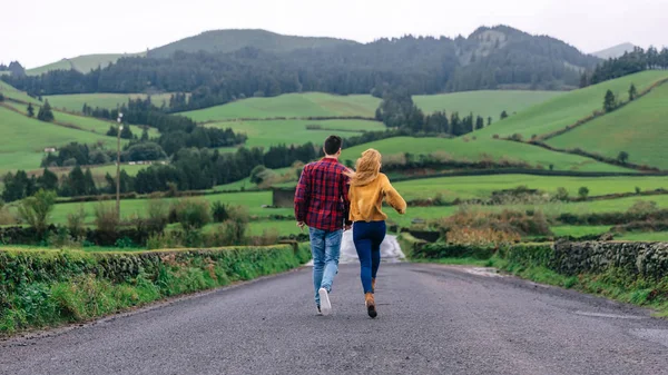Das verliebte Paar hält sich an den Händen und rennt die Straße entlang. Berge — Stockfoto