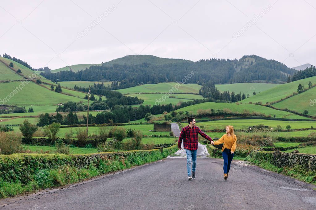 guy and girl holding hands and look at each other. mountains and