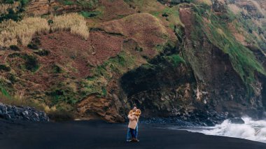 Birbirine aşık bir çift, OC yakınlarındaki kayaların arka planında sarılır.