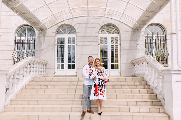 Recién casados en ropa bordada abrazo en las escaleras cerca del edificio —  Fotos de Stock