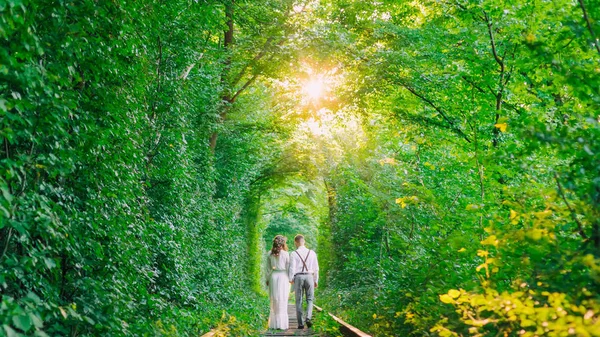 Le couple amoureux se tient la main et marche. un tunnel arboré et un rail — Photo