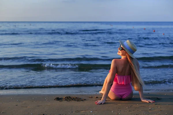 Menina sentada na praia em maiô rosa e velejador. a ver — Fotografia de Stock