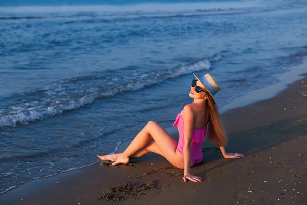 Το κορίτσι κάθεται στην άμμο δίπλα στη θάλασσα και χαμογελάει. κορίτσι σε ροζ SWI — Φωτογραφία Αρχείου