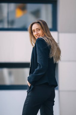 Siyah takım elbiseli kız poz veriyor ve elini saçında tutuyor. s