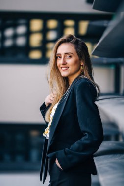 Siyah takım elbiseli kız poz veriyor ve elini saçında tutuyor. s