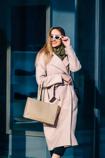 Stijlvolle vrouw in een jas en zonnebril in de buurt van de winkel — Stockfoto