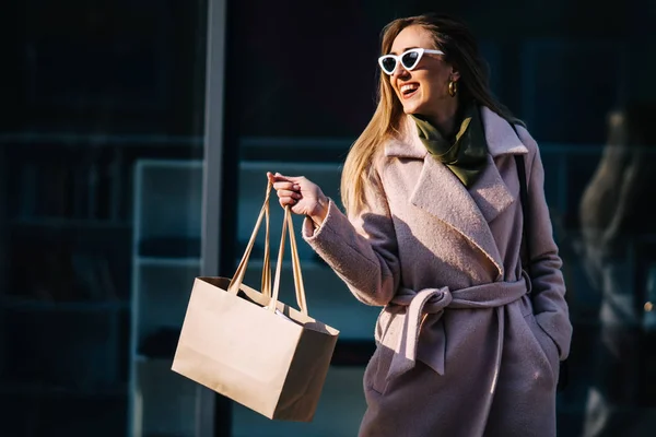Uma mulher elegante em um casaco e óculos de sol nas compras. loja windo — Fotografia de Stock