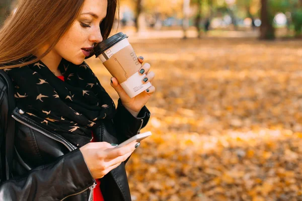 Mujer joven en una chaqueta de cuero y bufanda bebiendo café y ho. — Foto de Stock