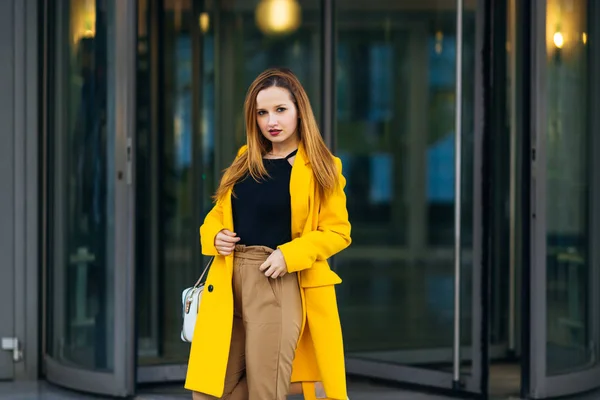 Уличный стиль. девушка в желтом пальто смотрит в камеру на — стоковое фото