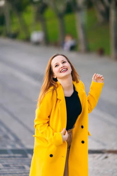 Giovane ragazza elegante che indossa cappotto giallo moderno. sorridere. città stree — Foto Stock