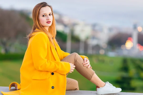 Una ragazza in un cappotto giallo guarda la macchina fotografica e posa contro th — Foto Stock
