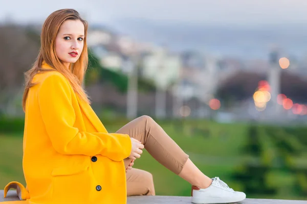 Una ragazza in un cappotto giallo guarda la macchina fotografica e posa contro th — Foto Stock