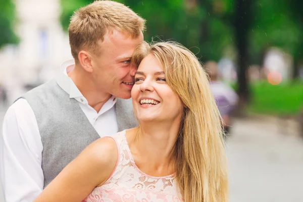 En kille viskar något till flickans öra och hon ler. Park. — Stockfoto