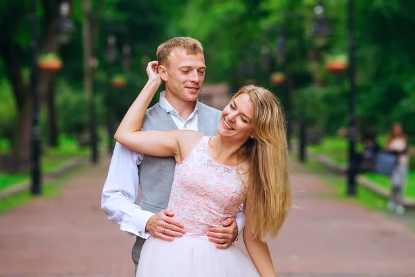 Ο γαμπρός αγκαλιάζει τη νύφη από την πίσω πλευρά. Χαμογέλα. πάρκο. — Φωτογραφία Αρχείου