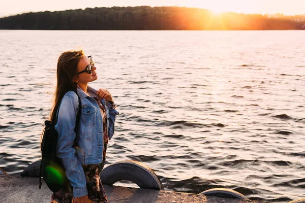 Profil eines Mädchens mit Rucksack und Sonnenbrille am Ufer des — Stockfoto