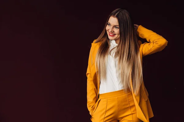 Girl with long hair in a stylish yellow suit poses against the b — Stock Photo, Image