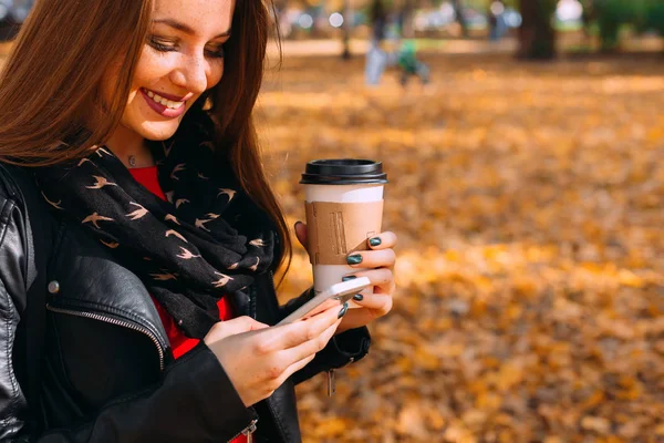 A beautiful girl in a leather jacket smiles and holds a cup of c