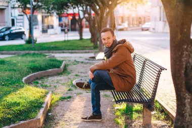 Şık giyinmiş sakallı esmer, bankta oturuyor. iyi akşamlar 