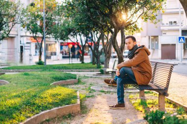 Şehir caddesinde küçük bir park. Adam bankta oturuyor. poz.