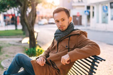 Ceketli sakallı bir adam bankta oturuyor ve ona bakıyor.