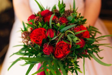 Gelin elinde kırmızı şakayık ve yeşil yapraklardan bir buket tutuyor..