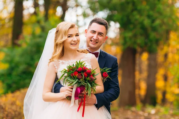 De bruidegom knuffelt de bruid van achteren. bruid houdt bruiloft — Stockfoto