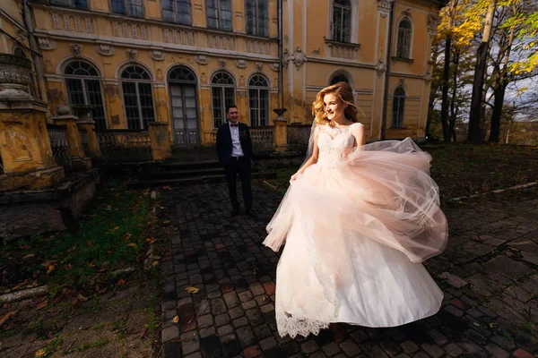 Невеста в свадебном платье бежит по тротуару. groom on the backgro — стоковое фото