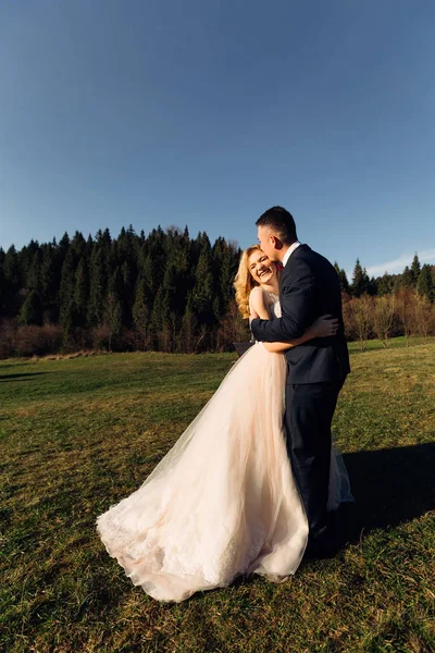 Le mari embrasse et embrasse la mariée sur une pelouse près de la forêt. smile — Photo