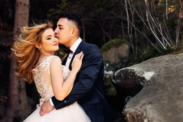 Yeni evliler nazikçe sarılır, gözlerini kapatır ve gülümserler. kayalar.