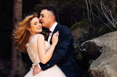 Yeni evliler nazikçe sarılır, gözlerini kapatır ve gülümserler. kayalar.