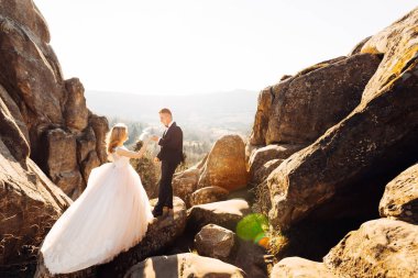 Damat gelinin elini kayalıkların arasında tutuyor. Yeni evliler.