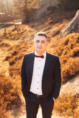 Siyah takım elbiseli damat ellerini cebinde tutuyor ve...