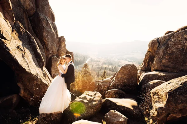 Penhasco com vista para as montanhas. os recém-casados estão abraçando cada um — Fotografia de Stock