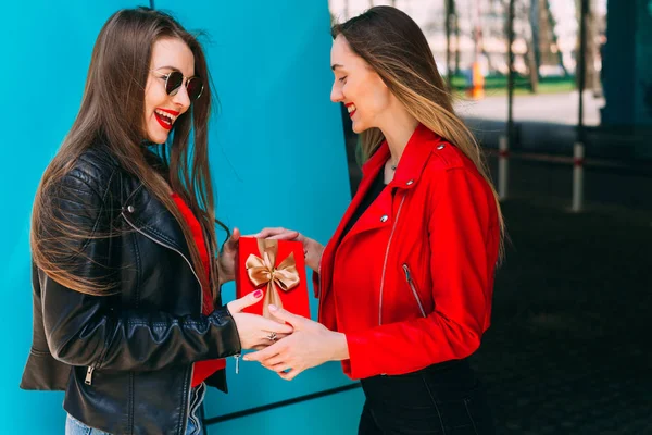 Ragazza in una giacca di cuoio e occhiali da sole dà una scatola con nastro a — Foto Stock