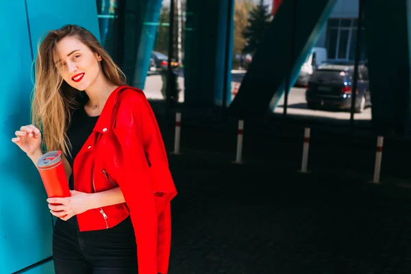 Meisje in stijlvolle kleding houdt rood een thermische mok en kijk naar camer — Stockfoto