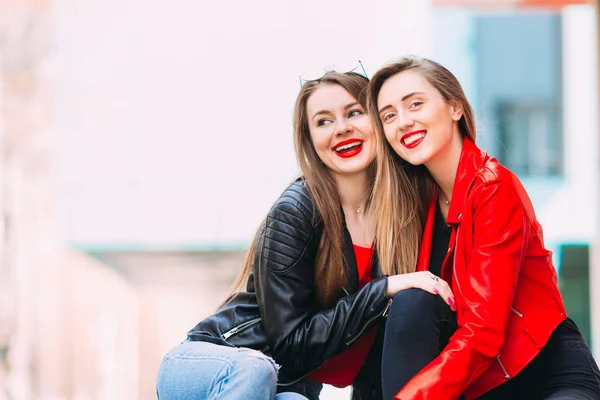 Chicas elegantes en chaquetas de cuero sentadas y sonrientes. Plaza de la ciudad — Foto de Stock