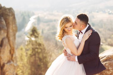 Güzel yeni evliler sarılıyor, kayaların arkasında, ston