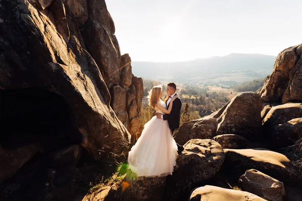 Penhasco com vista para as montanhas. os recém-casados estão abraçando cada um — Fotografia de Stock