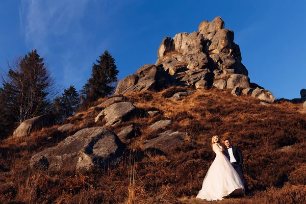Nouveaux mariés en vêtements de fête sur fond de falaise et de ciel — Photo