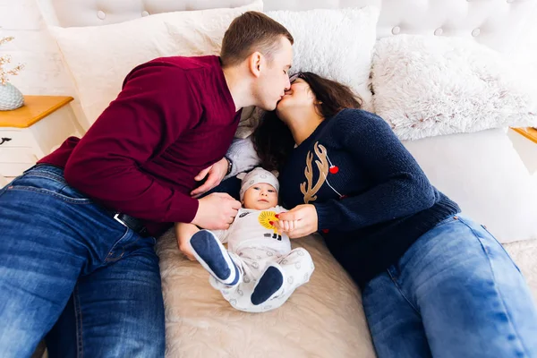 Parents lie on the bed in the bedroom and kiss and between them — Stock Photo, Image