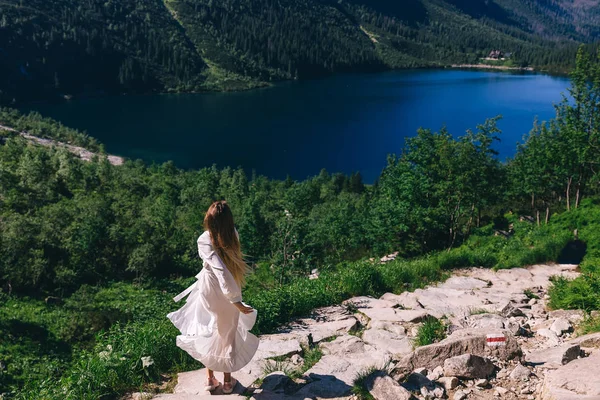 Beyaz elbiseli kız dönüyor. gölün kayalık kıyısı. Fikret — Stok fotoğraf