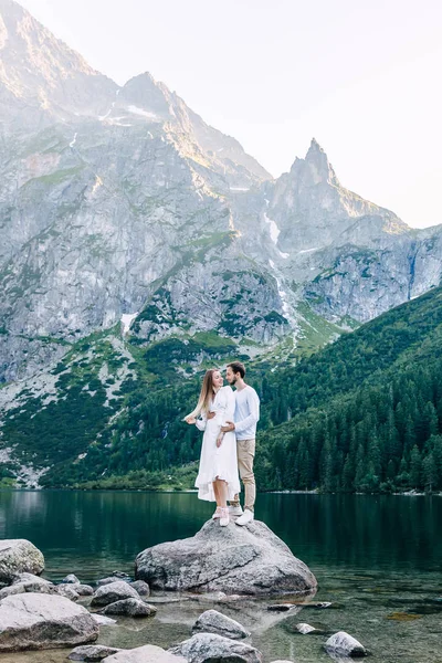 Mann und Mädchen umarmen sich auf Steinen zwischen See und Bergen — Stockfoto