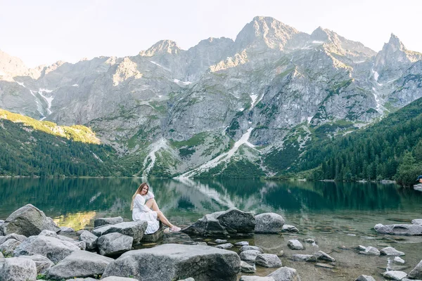 Beyaz elbiseli kız resimli bir gölün kıyısında oturuyor. — Stok fotoğraf