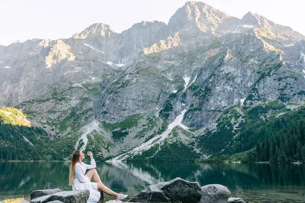 Menina em um vestido branco senta-se nas margens de um lago pitoresco s — Fotografia de Stock